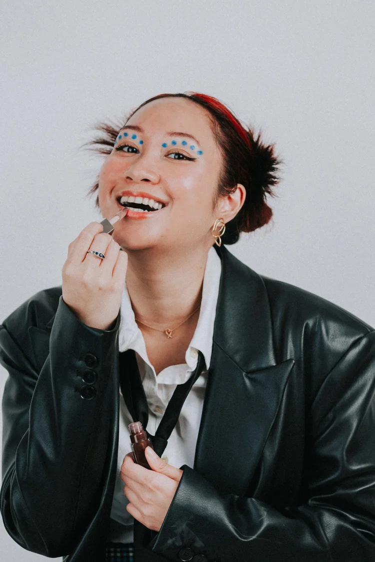 A smiling studio portrait applying lipstick