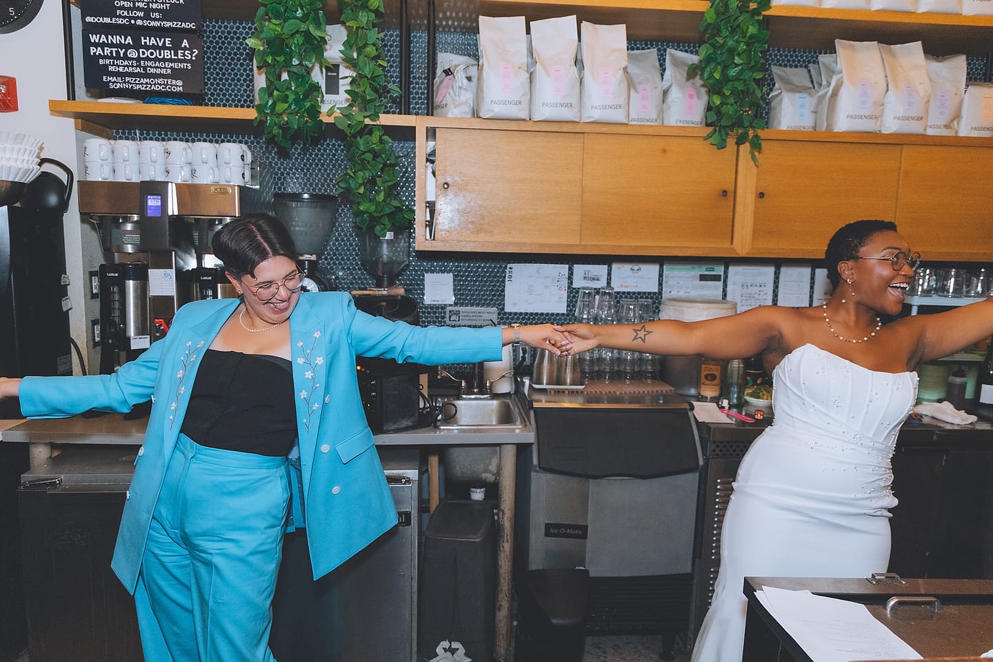 Two brides play behind a cafe counter at their urban Washington DC restaurant wedding