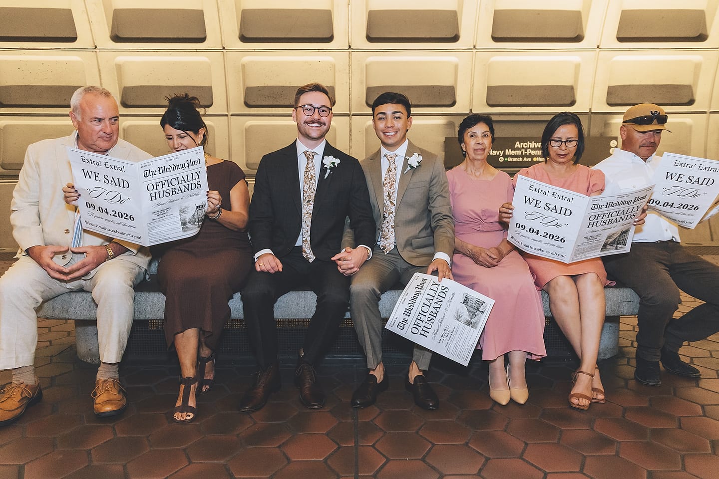 Marco and Nick with family holding custom 'Officially Husbands' newspapers on a bench at a Washington, D.C. Metro station