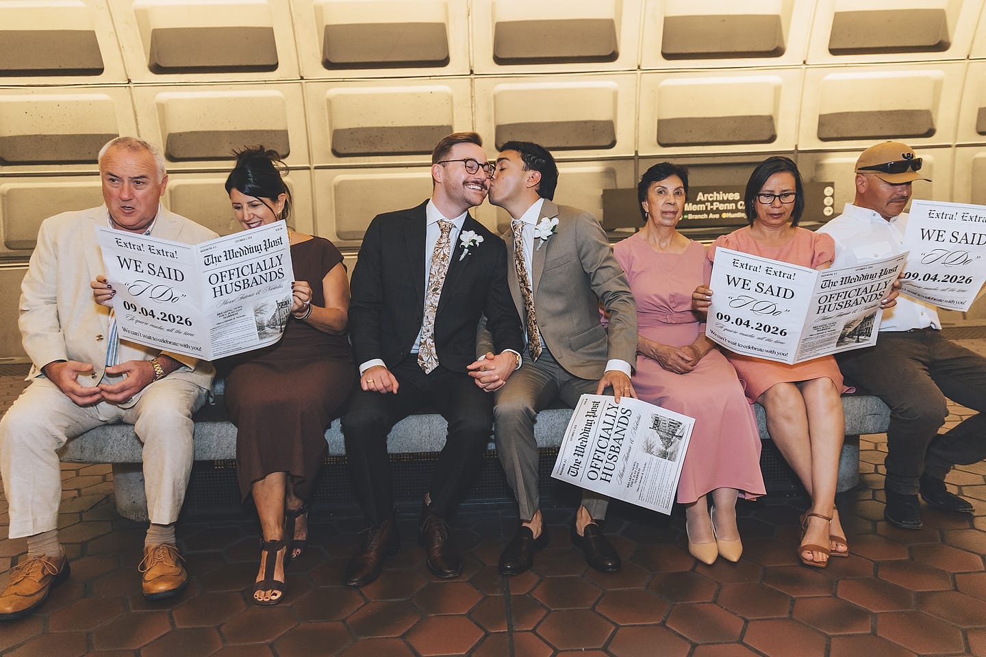 Marco and Nick kiss surrounded by family holding 'Officially Husbands' newspapers at a Washington, D.C. Metro station