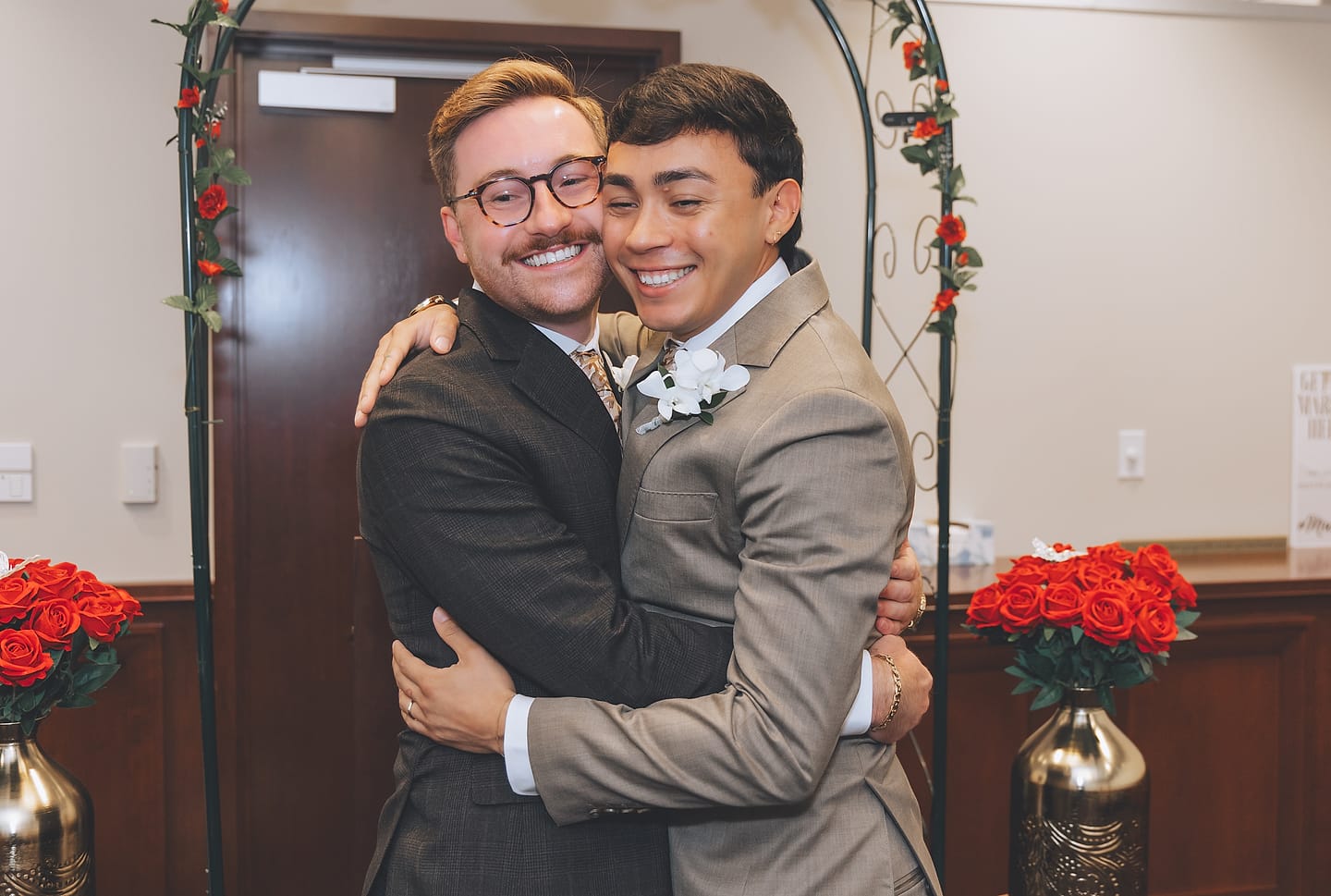 Marco and Nick share a warm embrace beneath a floral arch after their courthouse wedding ceremony in Washington, D.C.
