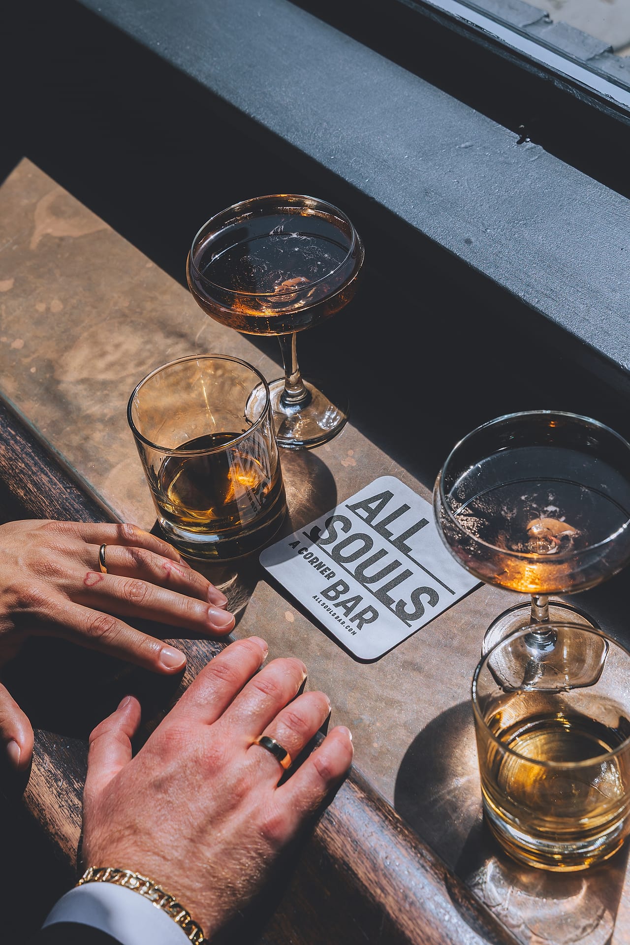 Close-up of Marco and Nick's wedding rings beside cocktails on an All Souls bar coaster in Washington, D.C.