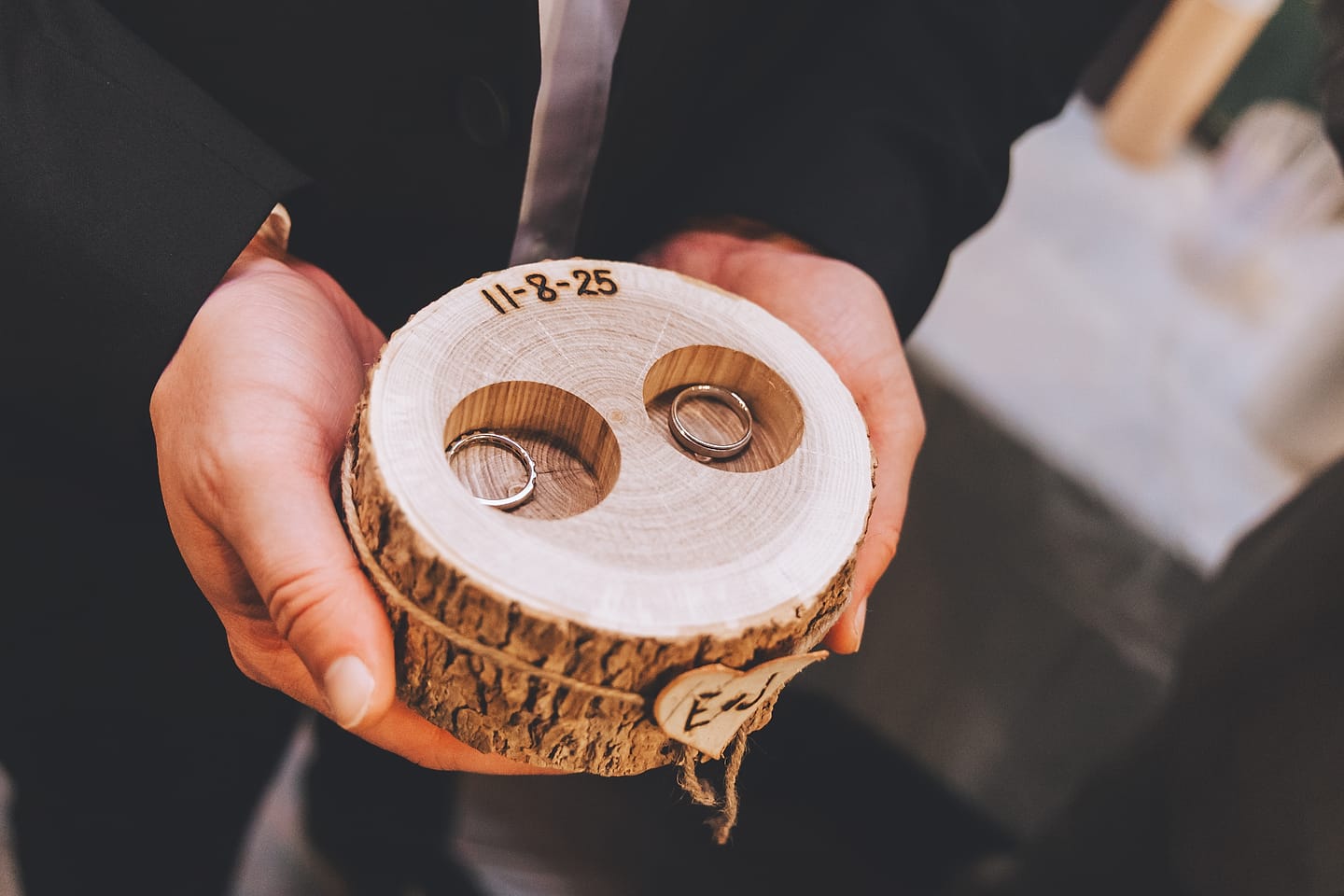 Two wedding rings in a wooden ring holder engraved with the wedding date