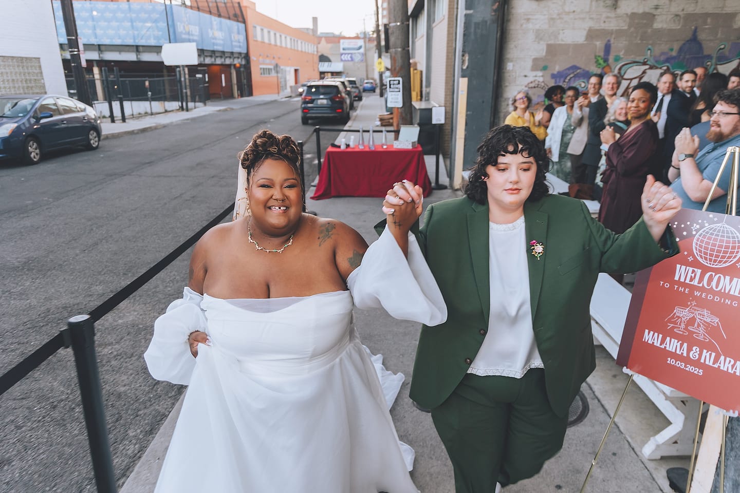 Two brides walk in hand in hand to cheering guests at their urban DC wedding