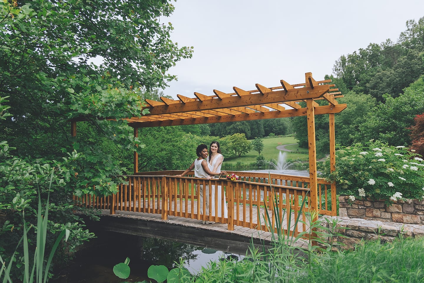 A couple embraces on a wooden garden bridge over a pond at their DMV wedding