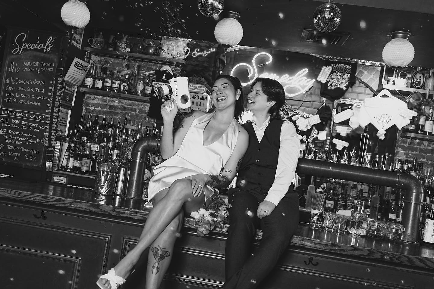 Newlyweds laugh at a lively bar reception, in black and white, at their DC wedding